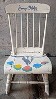 Front view of rocking chair showing painted seat design, spindle back, and signature on crest rail