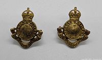 Front view of both brass Lincoln Welland cap badges showing design details