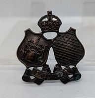 Front view of WW2 Loyola College COTC cap badge showing design and patina