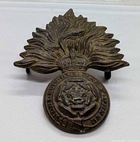 Front view of WW2 Canadian Royal Fusiliers brass cap badge showing flaming-grenade design and central emblem