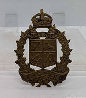Front view of brass cap badge showing crown, wreath and shield