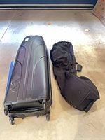 Hard shell case and soft bag side by side showing size and wheels