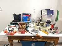 Overall view of assorted tools, hardware and supplies on table with blue tote beneath
