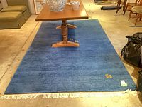 Full view of blue wool rug showing white fringe and animal motif, table placed on top