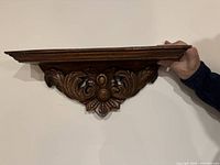Front angled view of carved wood wall shelf held against wall