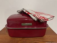 Front view of red KitchenAid covered roaster with linen towel folded on lid