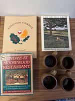 Front covers of three Moosewood cookbooks and four matching stoneware mugs