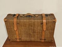 Front view of woven rattan suitcase with leather straps and metal hardware