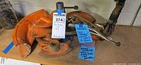 Orange pipe-bender dies, blue bottle jack, metal rod tools on bench