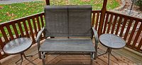Front view of metal loveseat glider with two round side tables on deck