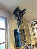 Conduit bender hanging from ceiling hook showing mounting plate and handle