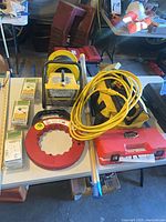 Overall lot on table showing tool bag, crimper case, fish tape, fiberglass rods, wiring kits, shop light, coil of cable
