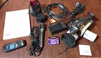 Full lot layout showing camcorder, charger, cables, mic, remote, tape, manual, lens accessories