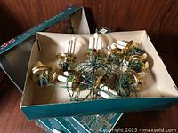 Open box showing green-wired string with white candle bulbs and brass socket cups