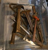 Assorted hand tools in plastic bin showing hammers, wrench, pry bar, files, locking pliers
