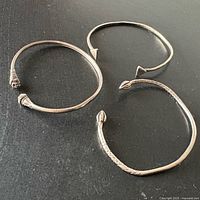 All three sterling silver bangles laid flat on dark surface