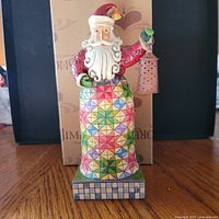 Front view of Jim Shore Santa figurine with lantern and box behind