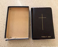 Bible and box on countertop, showing black cover with gold cross and name, box interior visible