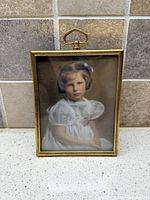 Framed portrait standing against tiled background, full view of brass frame and hanging loop