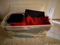 Overall view of clear plastic bin showing folded garments and bags