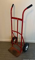 Full view of red steel two-wheel hand truck dolly showing handles, frame, wheels, and footplate