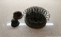 Three metal flower frogs on countertop: large hair-pin style and two smaller pin styles