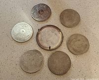 Seven silver coasters laid out, six flat and one footed base