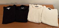 Four folded Pendleton sweaters, two black and two cream, showing overall quantity and color