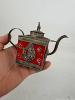 Front view showing porcelain body, metal frame, handle, spout and horse-finial lid