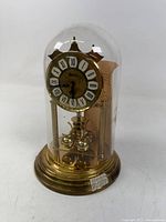 Full view of brass anniversary clock under glass dome on base