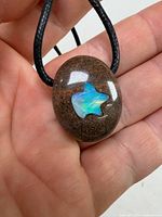 Front view of oval brown stone pendant with star opal inlay on black cord