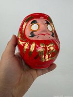 Front view of red papier-mâché Daruma showing gold 福 character and facial features