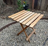 Three-quarter view of teak folding table showing slatted top and legs