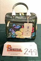 Front view of satchel showing floral artwork, handles, tags attached