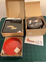 Three boxes containing square plates, covered serving bowl with pelican design, and low red interior bowl