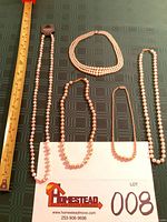 Five necklaces laid out with measuring tape for scale