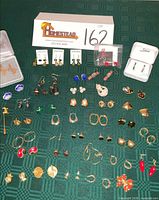 Full layout of approximately 40 pieces of earrings and pins on green fabric