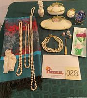 Lot overview showing vanity set, jewelry, shawl, doll, glass egg, thimbles, metal tray, sewing tool