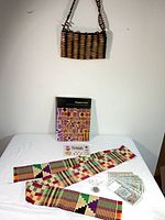 All items together on table including wooden handbag, book, kente sash, currency, coin, stickers