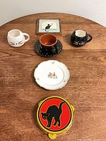 Lot overview showing mugs, tile, cup & saucer, plate, tambourine