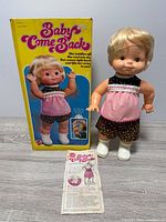 Front view of doll beside original box and instructions
