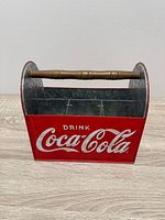 Front view showing red metal body, white Drink Coca-Cola logo, wood handle and interior dividers
