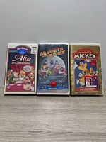 Front view of three sealed VHS tapes: Alice in Wonderland, Muppets from Space, The Spirit of Mickey