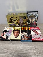 Front view showing Elvis Trivia Game tin, Graceland DVD, four VHS tapes front covers