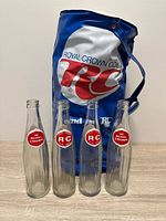 Four RC Cola glass bottles standing in front of blue vinyl cooler bag