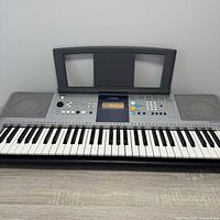 Front view of Yamaha digital keyboard showing keys, control panel, speakers, and music rest