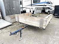 Front three-quarter view of flatbed trailer showing wood sides, tongue, coupler and single axle