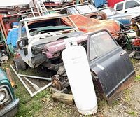 Overall view of stripped pickup truck cab, detached door, propane cylinder and surrounding scrap
