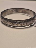 Side view of sterling silver engraved bangle showing floral pattern and safety chain