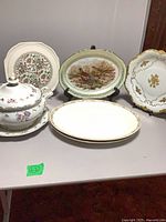 Five porcelain pieces displayed on table: tureen set, platter, three decorative plates